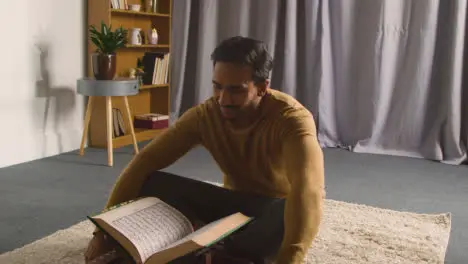 Muslim Man At Home Sitting On Floor And Reciting From The Quran 1