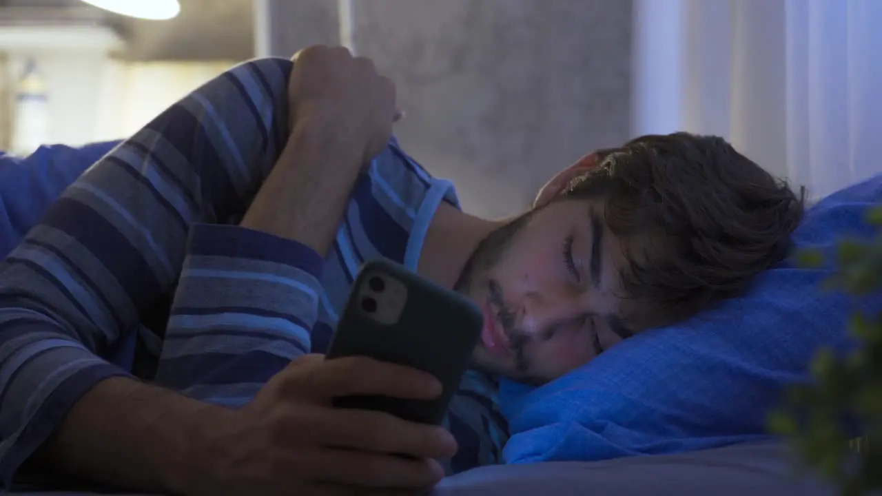 The man looking at the phone at night is dozing in his bed