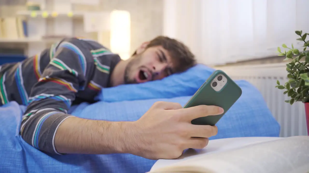 Young man looking at phone falls asleep in bed