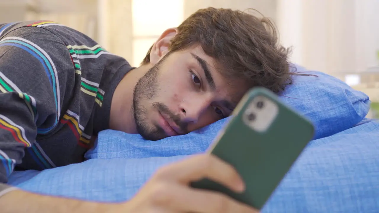 Young man playing on the phone falls asleep in bed