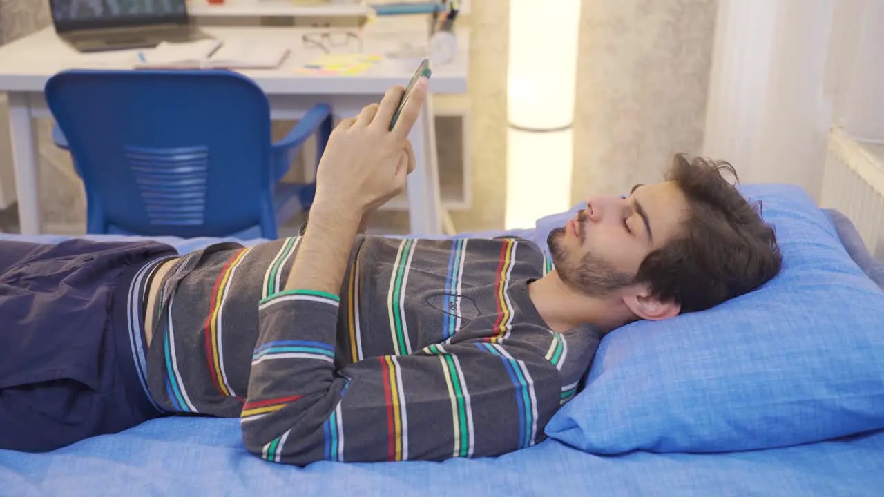 Sleepy young man looking at phone in bed