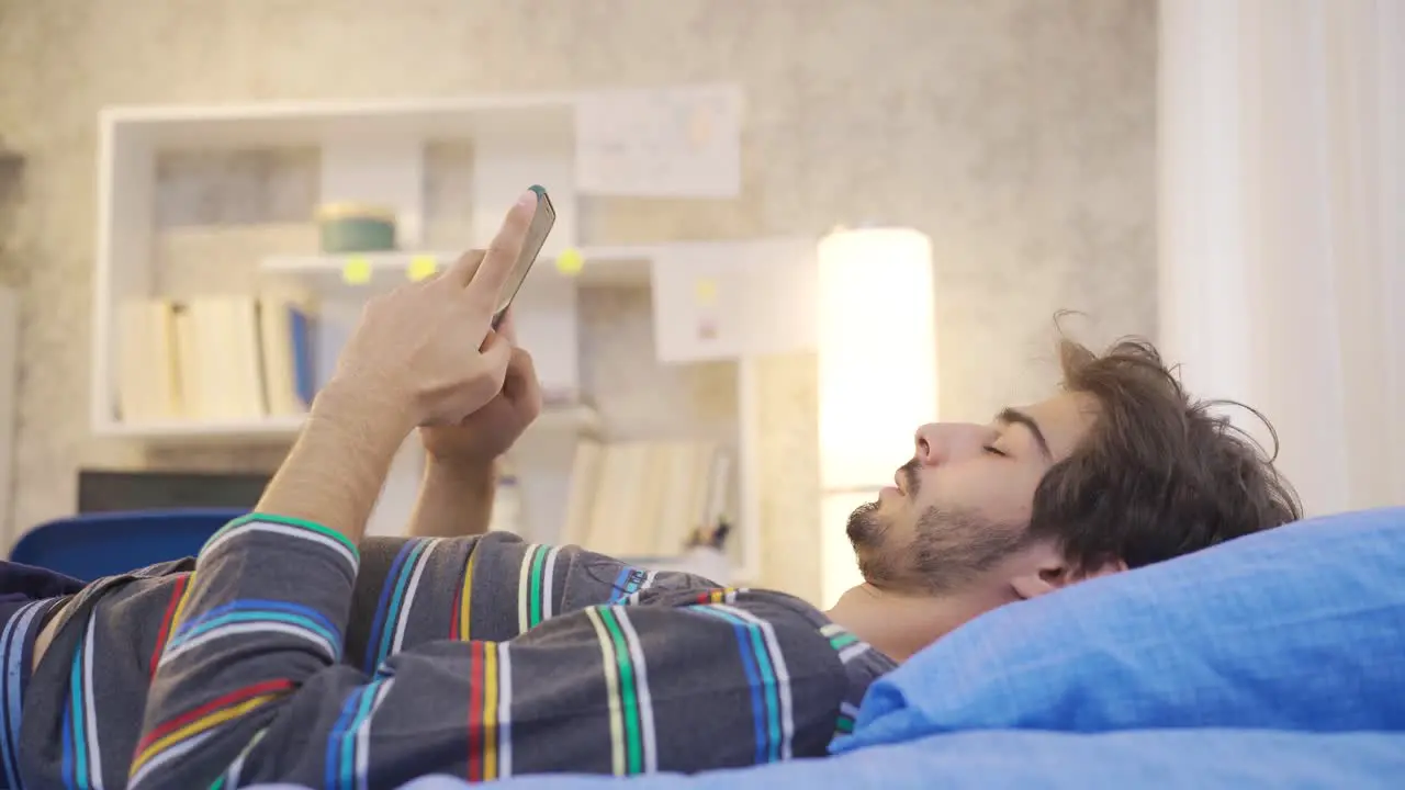 Phone addicted young man texting on the phone in his bed