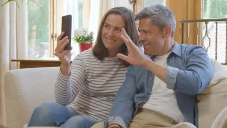 Sliding Shot of Middle Aged Couple Waving Goodbye into Smartphone During Video Call