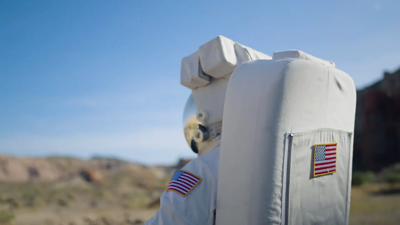 Astronaut looking around deserted terrain equipped with a mirroring visor and space gear