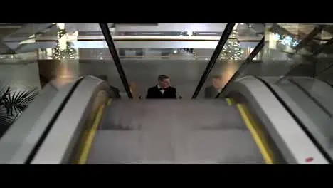 Young man in a black suit with bow tie coming up on the escalator in a shopping mall