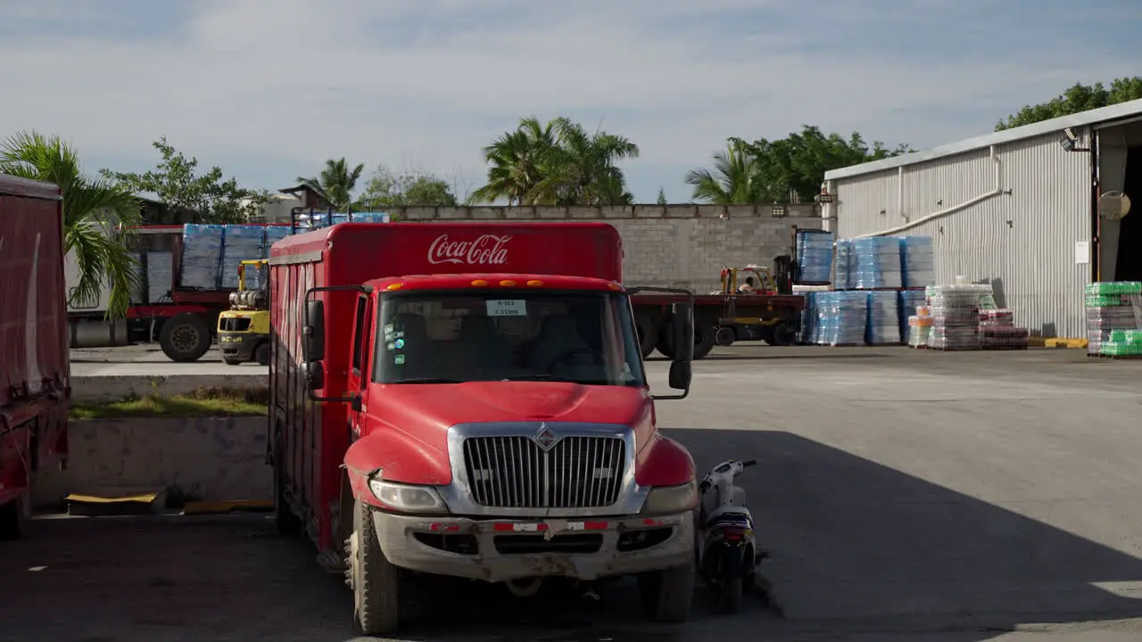 Stationary Parked Coca Cola Trucks At Distribution Centre In Punta Cana With Fork Lift Workers In Background