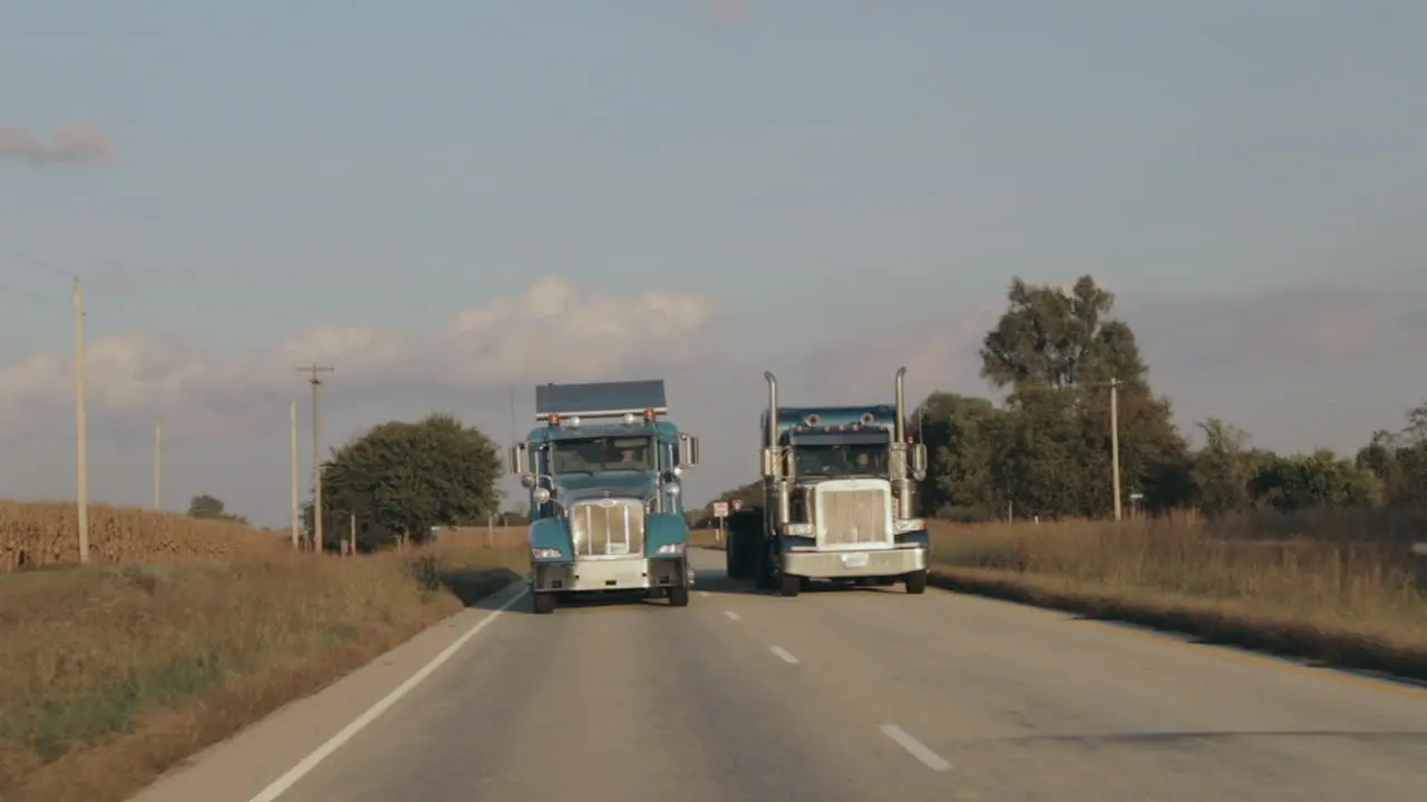 Two Peterbilt semi eighteen wheeler trucks driving down the highway in evening sun side by side in slow motion