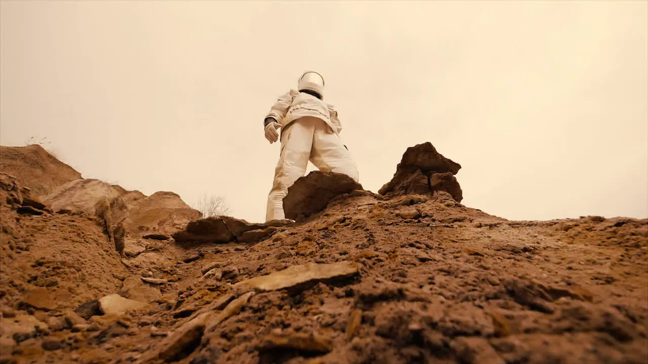 An astronaut wearing a spacesuit moving across a deserted planet with red soil looks off into the distance