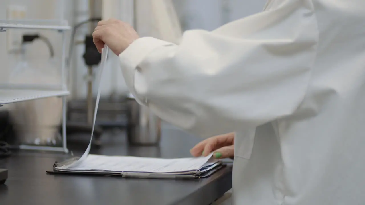 White coat female scientist in lab reading through research notes on a clipboard