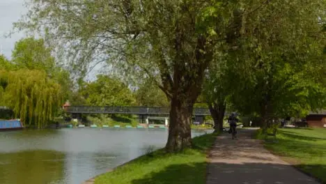 Tracking Shot of Cyclist Riding Along Path Next to River Cam