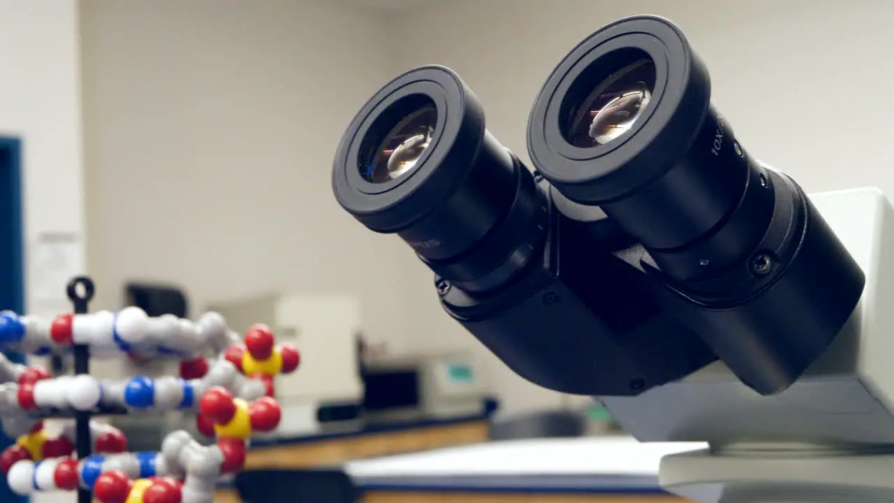 A student in a college biology science classroom doing an experiment behind a microscope and a dna double helix model