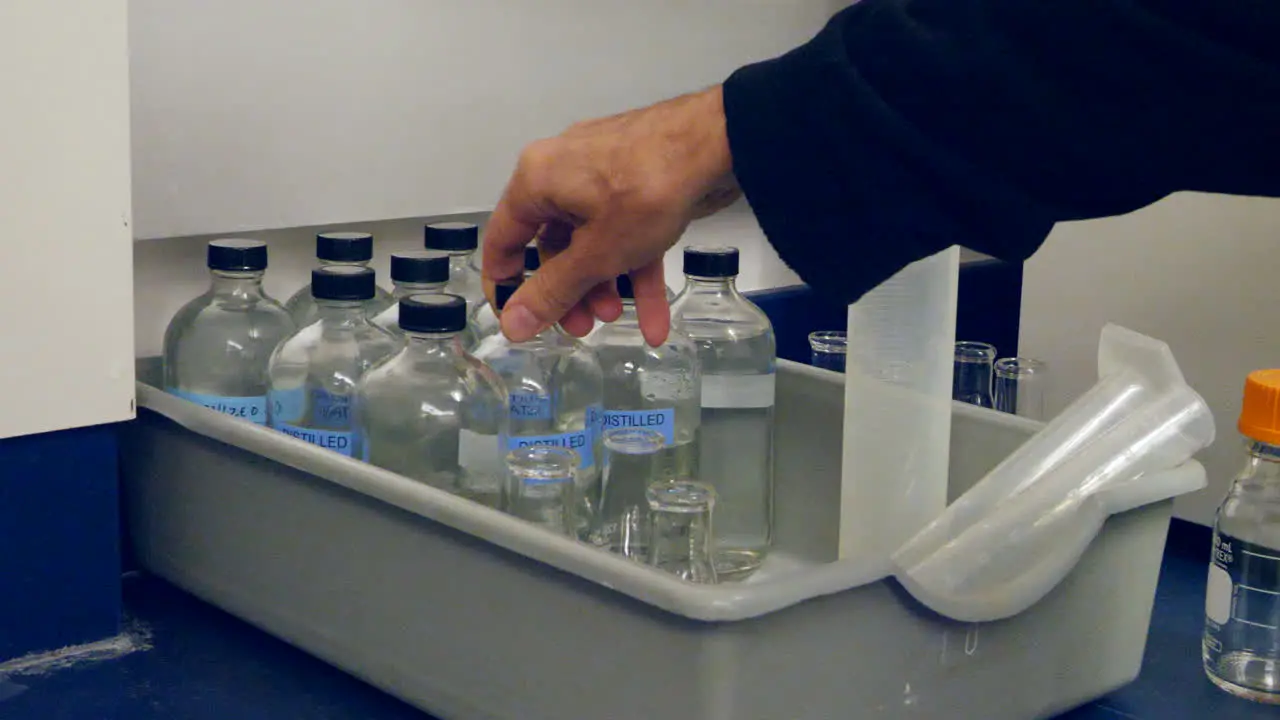 Close up on a scientist replacing a container of distilled water for an experiment in a medical research laboratory