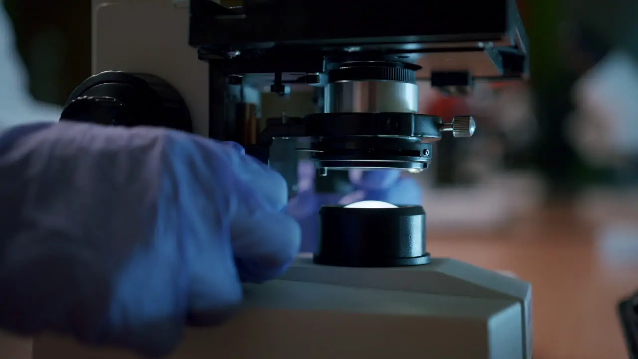 A young female scientist adjusts the professional microscope in the laboratory—a close-up shot of the microscope focusing block