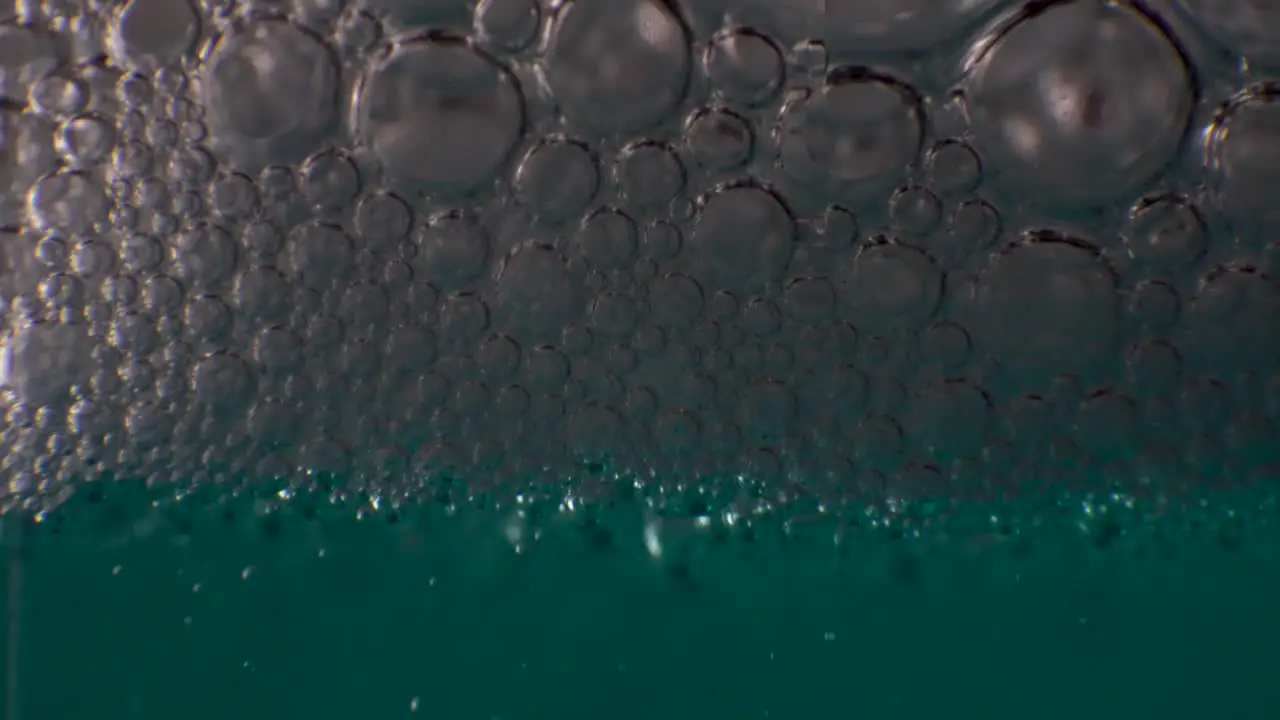 Thick layer of clear bubbles gathering on top of aqua colored liquid MACRO