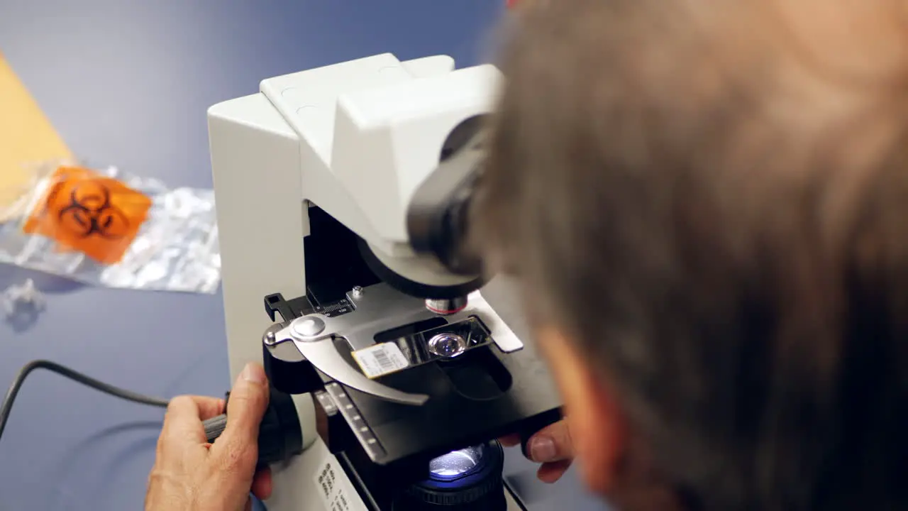 A scientist examining a slide with cancerous cells through a microscope in a medical research laboratory