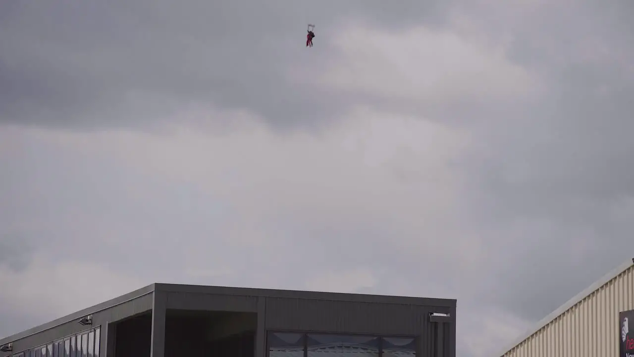 steady shot of an orange paraglider landing oever a building in wanaka