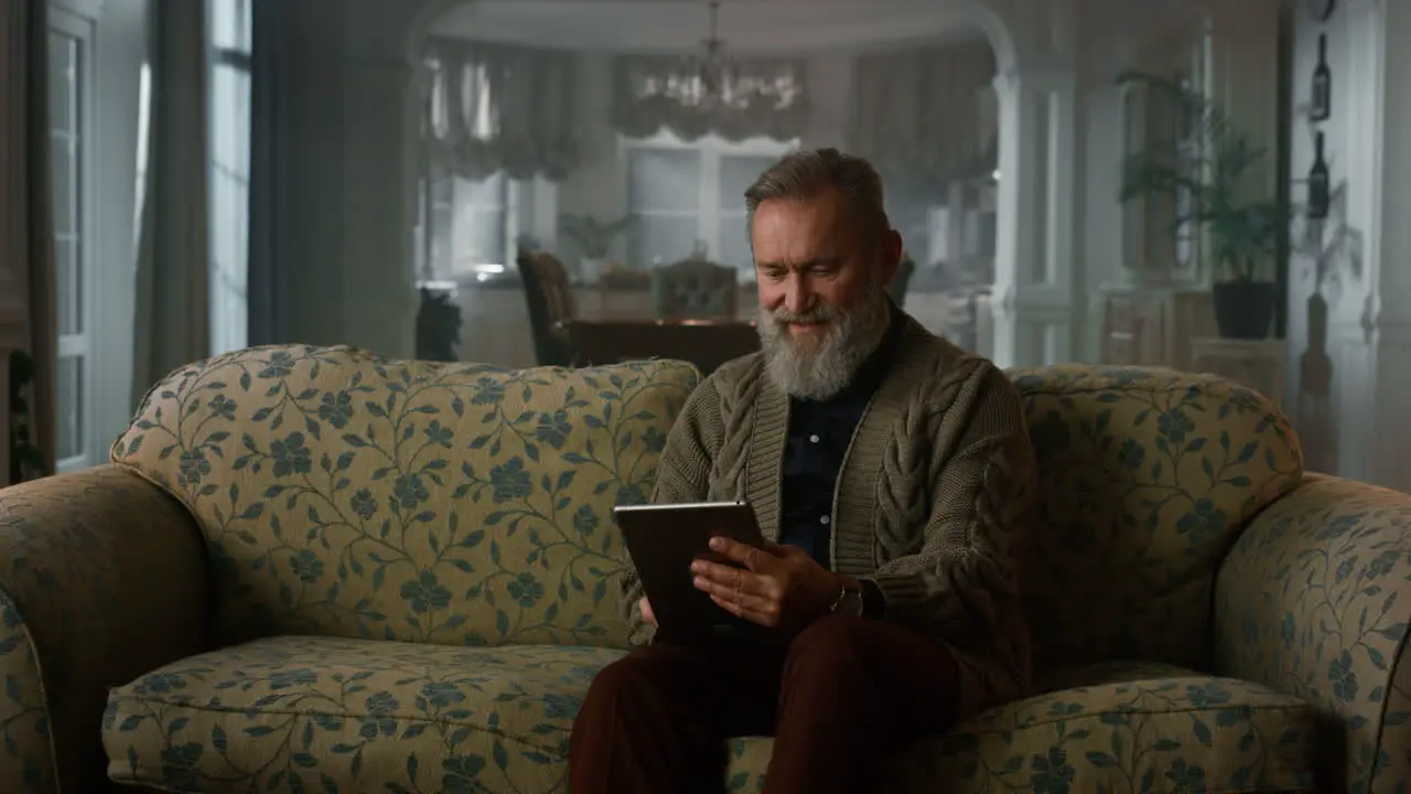 Calm senior man using tablet computer on sofa