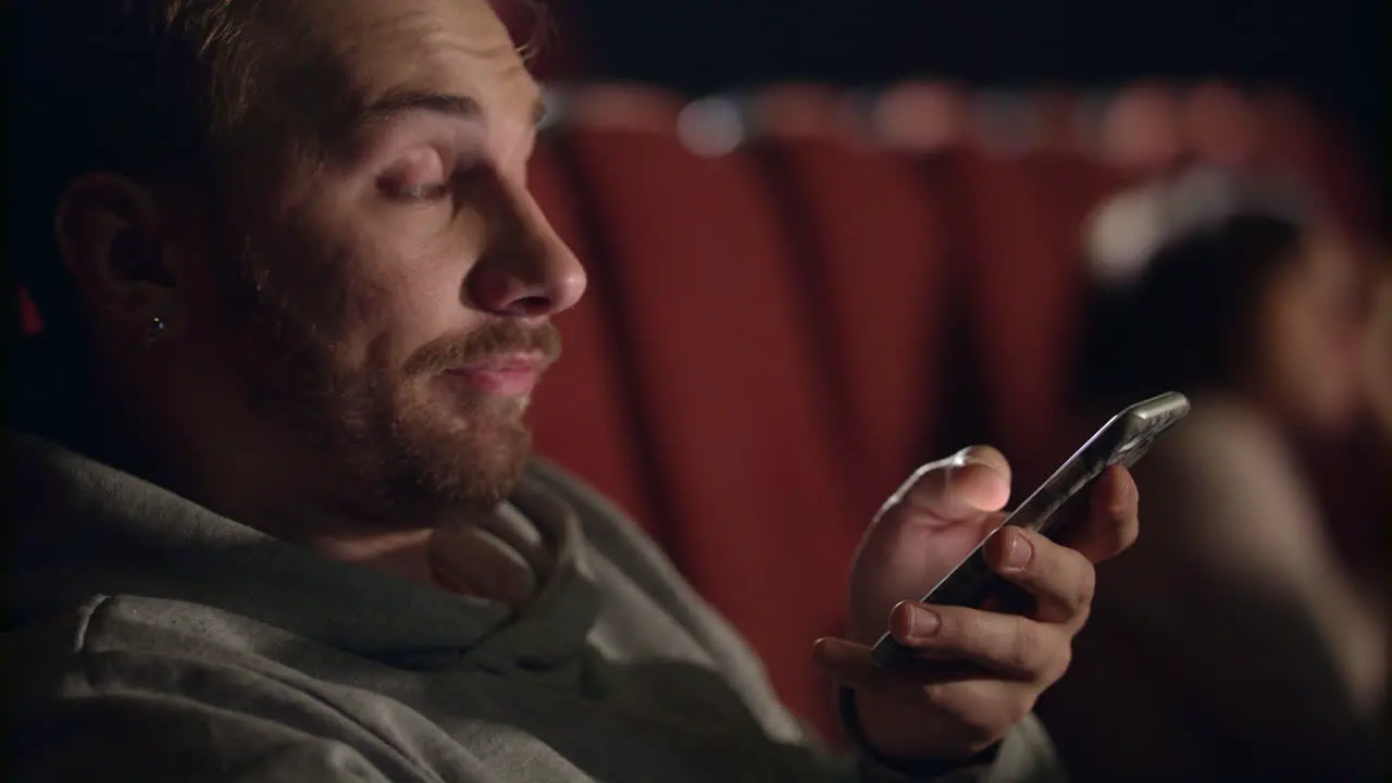 Yawning man using smartphone in the cinema