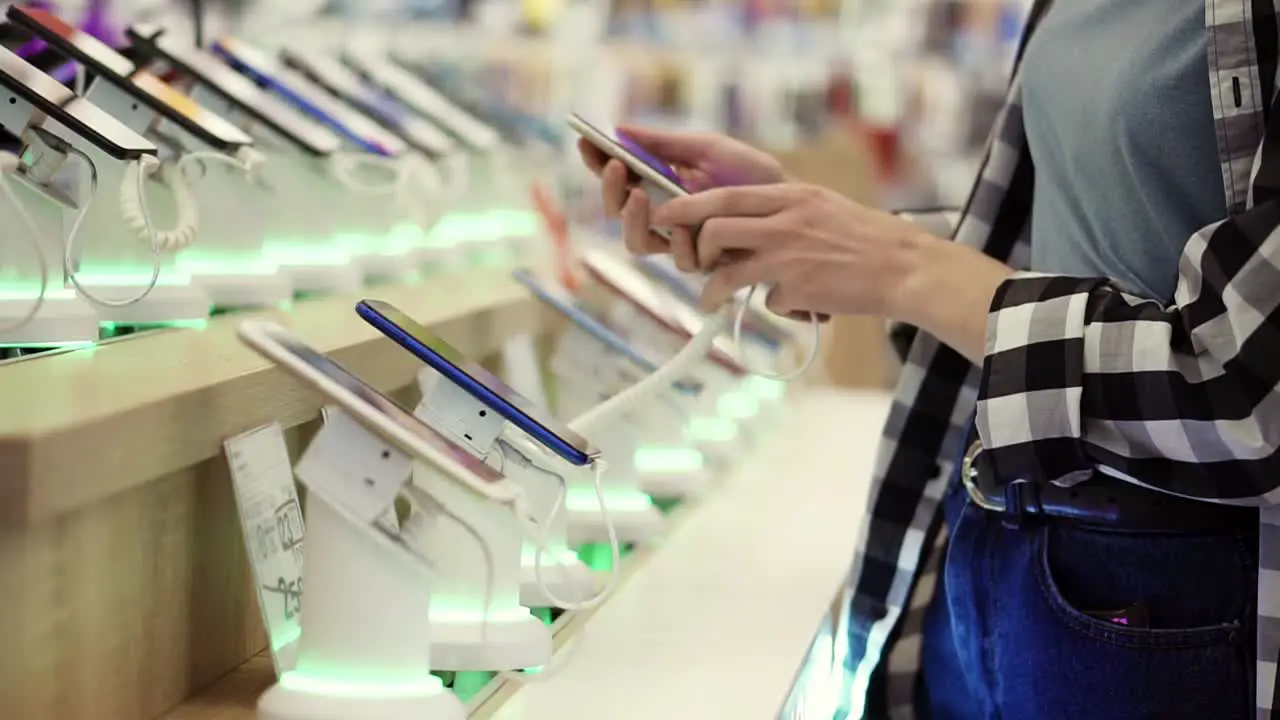 Waist Shot Of Unrecognizable Woman's Hands Chooses A Smartphone In An Electronics Store