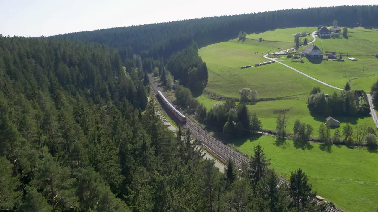 Aerial view of a red Deutsche Bahn train traversing lush green landscape with dense forests and rural homes in daylight