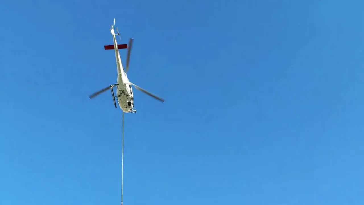 Helicopter over high alpine wooden cabin transporting cargo on a long steel rope down the valley