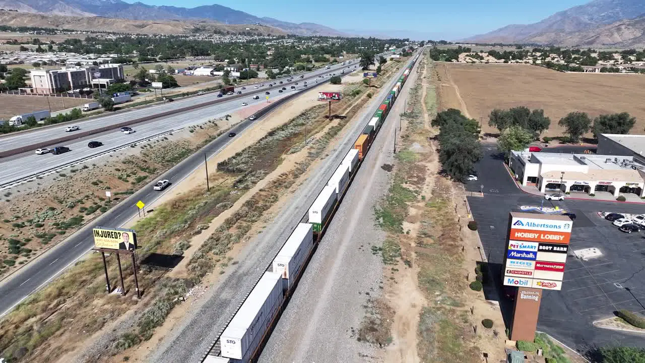 california metro link train carrying cargo through a mountain city in the desert AERIAL DOLLY PAN