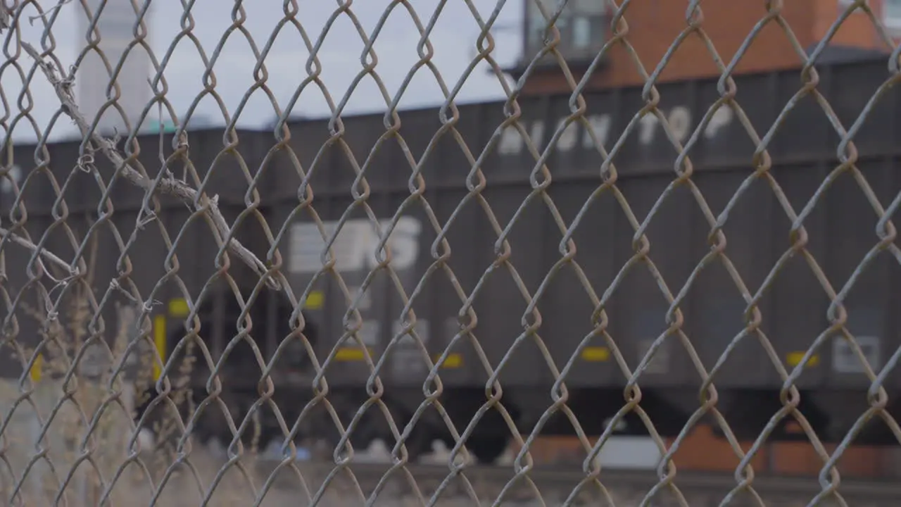 train cars and oil tankers passing through shot from behind chain link fence