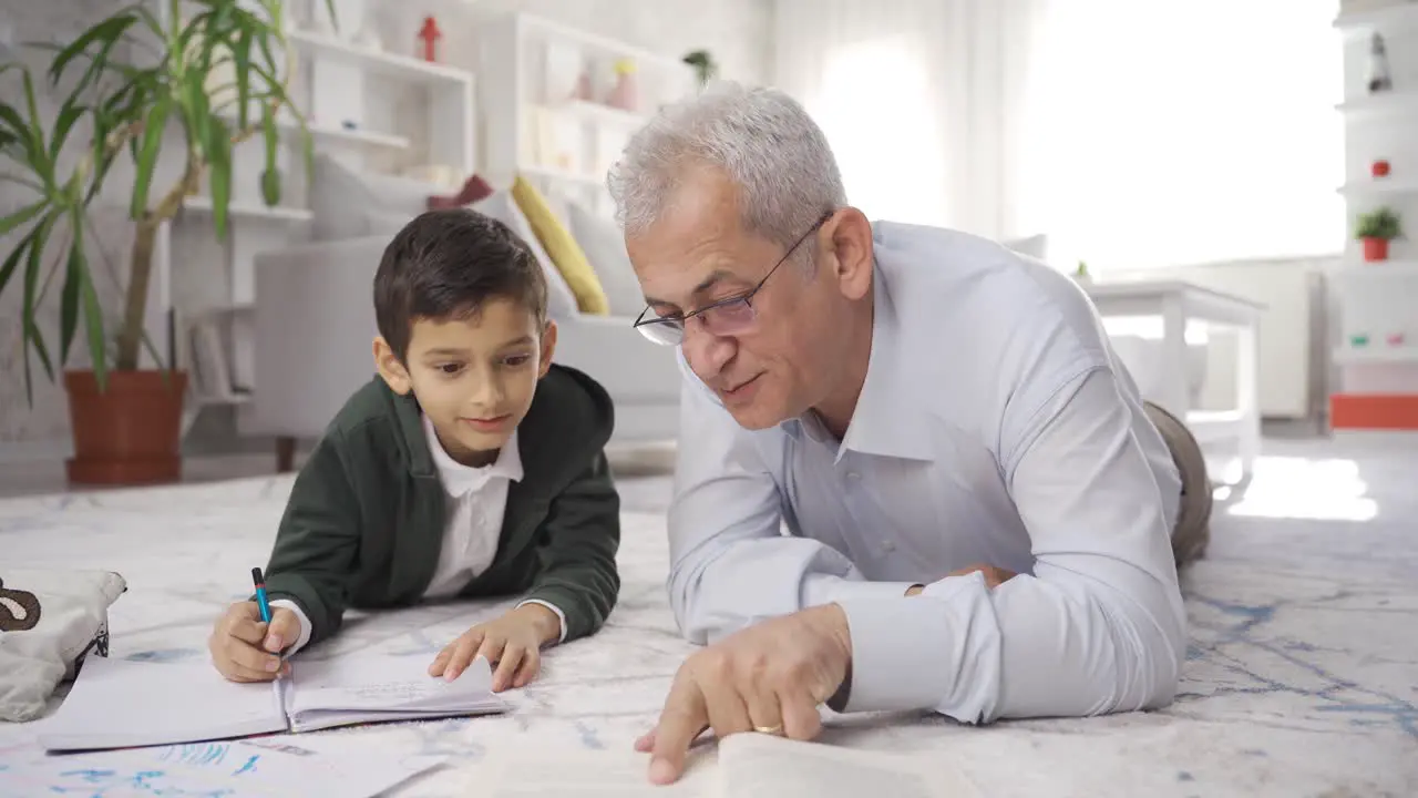 Mature father lying on the floor at home and helping his son with his studies