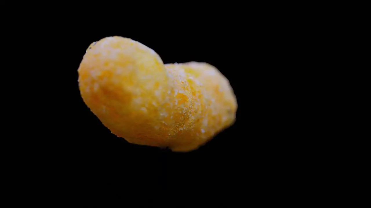 Cheesy Puff Snack Food Turning Slowly Isolated On Black Background close up