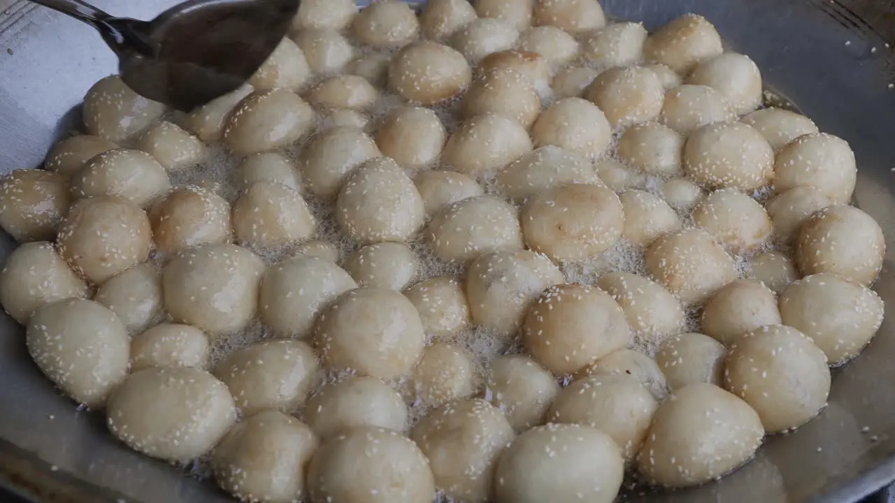 Street food vendor deep-frying sesame seed balls a type of Chinese pastry made of glutinous rice flour with green bean paste filling and covered with white sesame seeds in hot oil in large pan