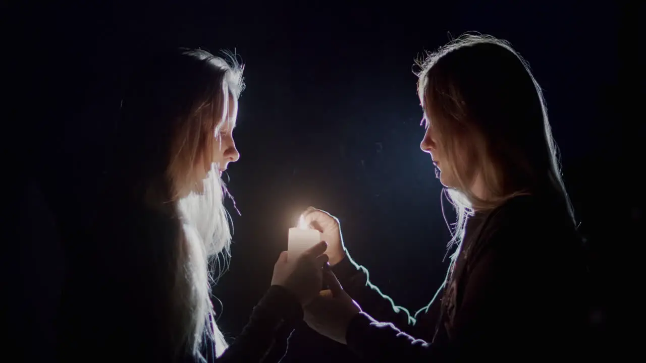 Mom and daughter light a candle in the dark look at the flame