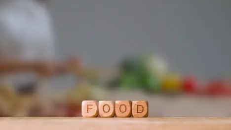 Concept With Wooden Letter Cubes Or Dice Spelling Food Against Background Of Woman Chopping Ingredients