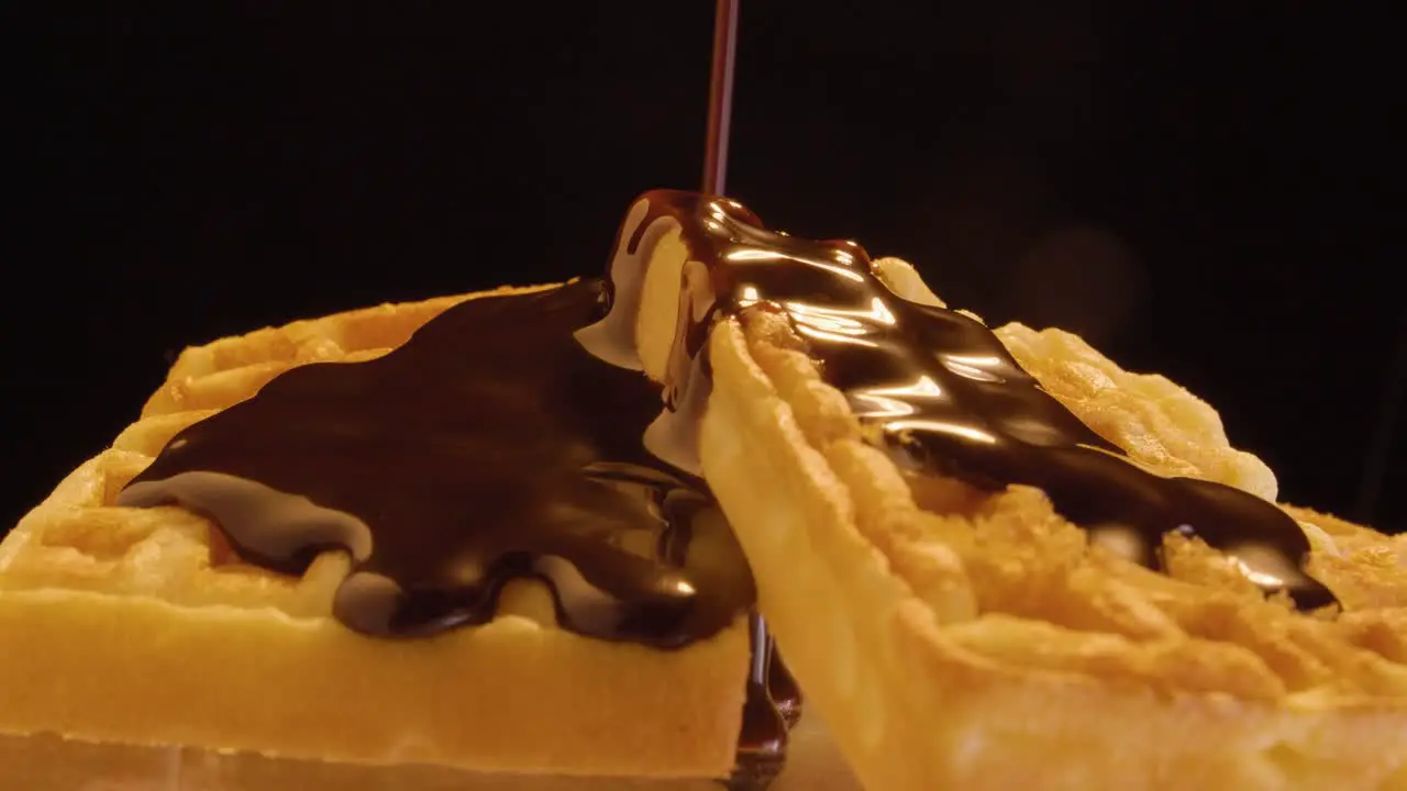 Static shot of delicious waffles with vegan chocolate sauce flowing down against a black background