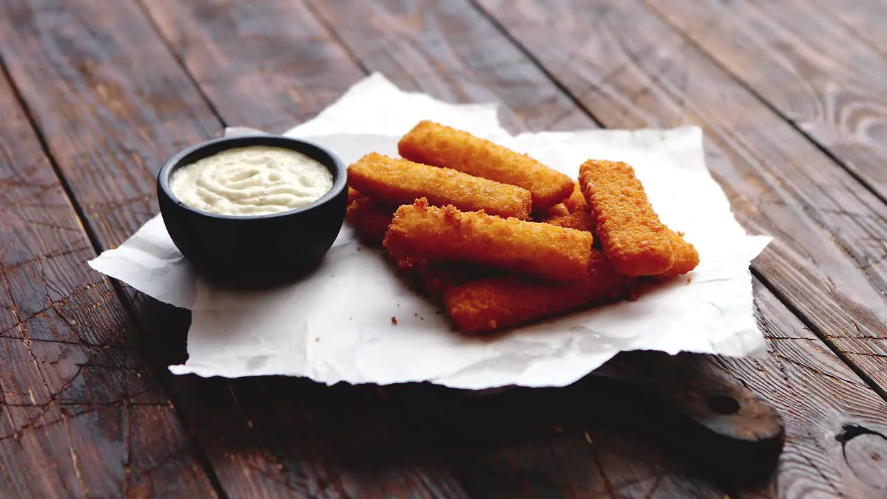 Pile of golden fried fish fingers with white garlic sauce