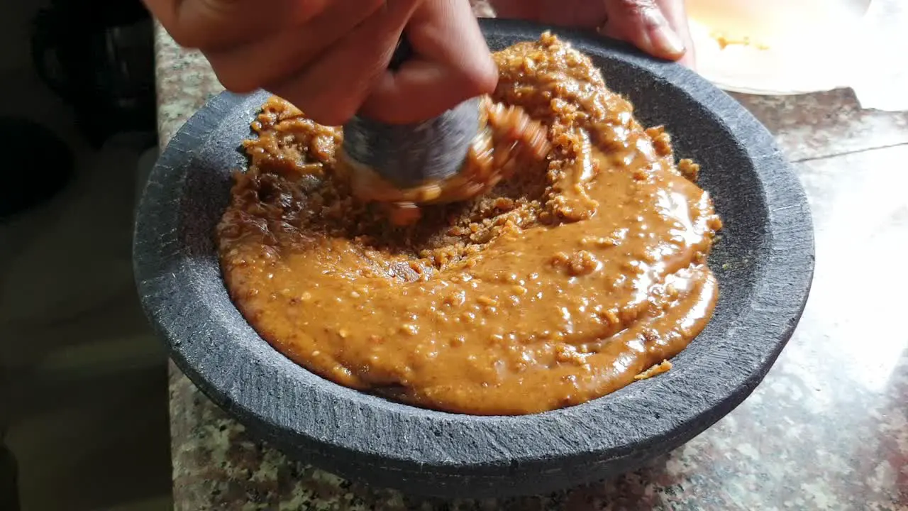 Palm sugar and ingredients being mashed into sweet sticky syrup with mortar and pestle close up of food preparation action