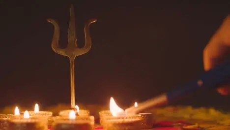 Hand Lighting Tea Lights Around Metal Trishula Statue Divine Trident Symbol Of Hinduism On Decorated Table