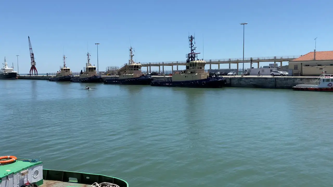 a couple of lovers canoeing in the sea port of alcantara on a sunny day with some armed forces ships in the background