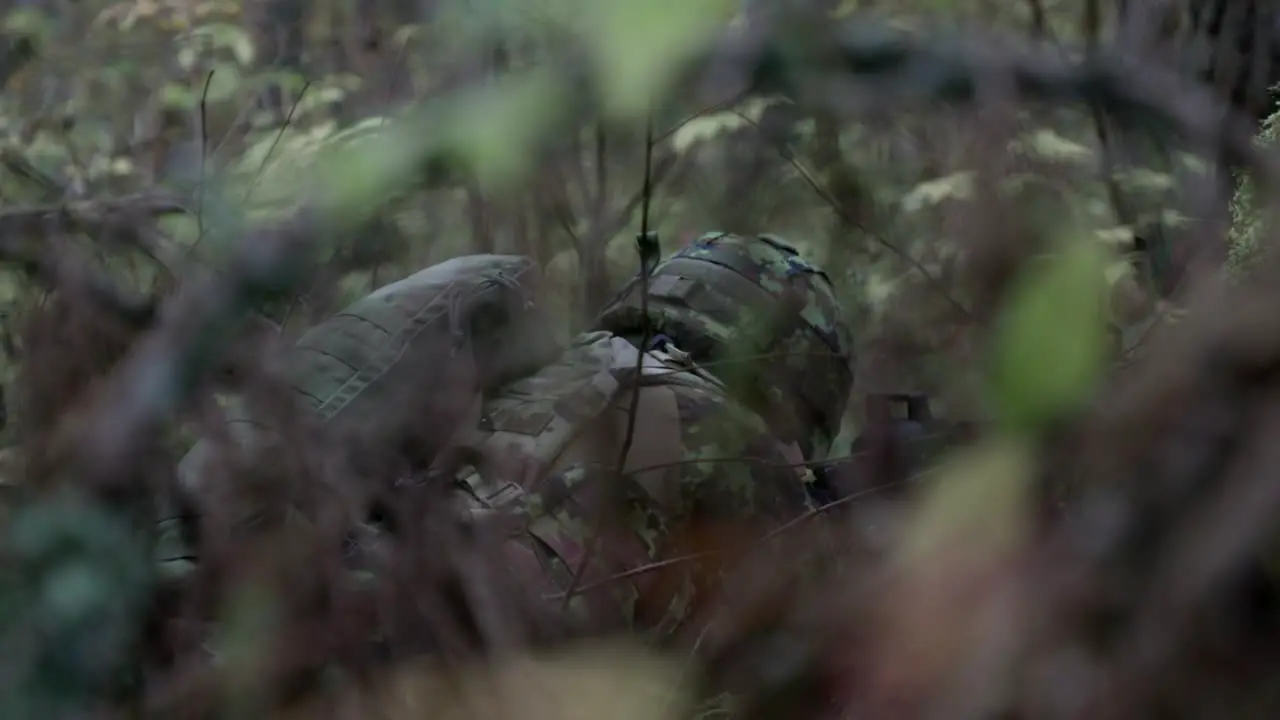 Soldier lying down stalking in the forest midshot behind slow motion