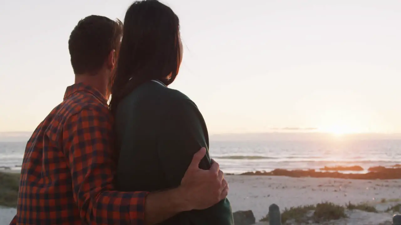 Happy caucasian couple sitting on beach by the sea talking hugging