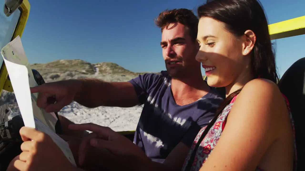 Caucasian couple sitting in beach buggy by the sea reading a map