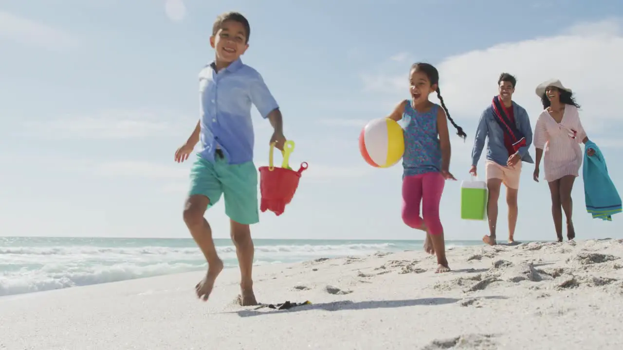 Happy hispanic family children and parents on beach carrying things