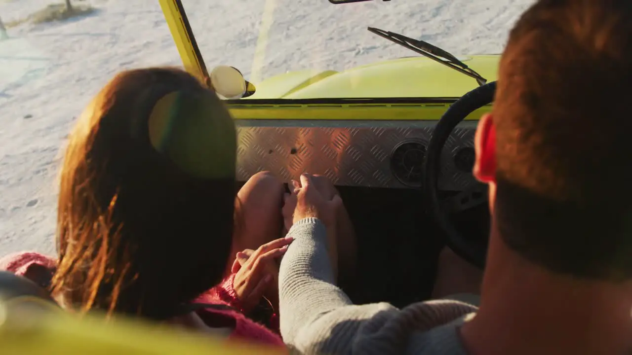 Happy caucasian couple sitting in beach buggy by the sea hugging