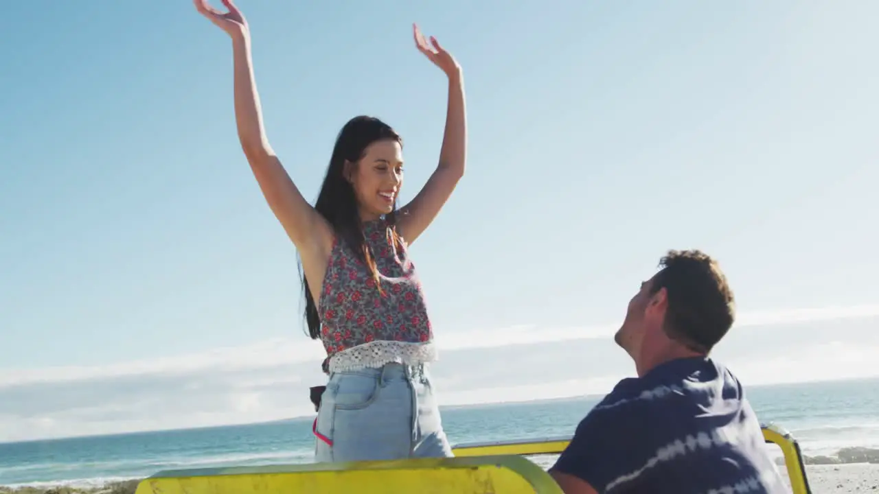 Caucasian couple sitting in beach buggy by the sea talking and dancing