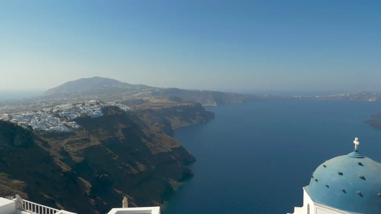 Pan up view over iconic caldera and blue rooftop church Santorini Greece