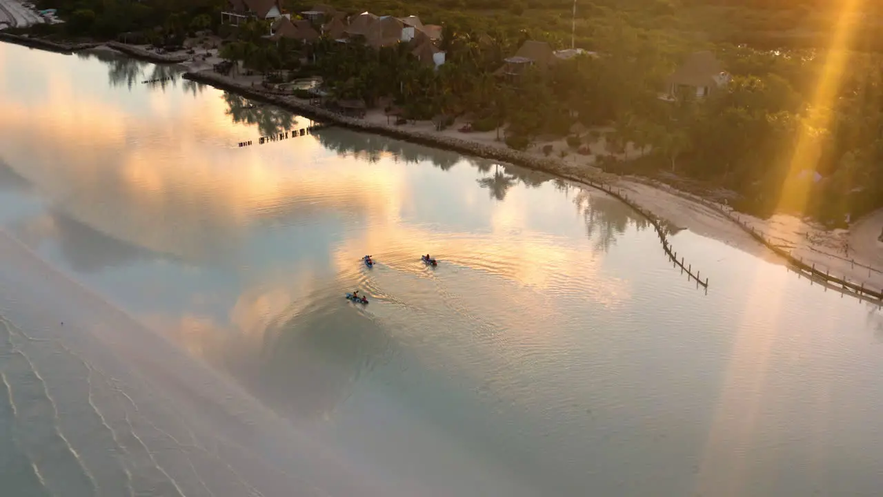 People paddling kayaks along beach at sunset clouds reflecting in sea