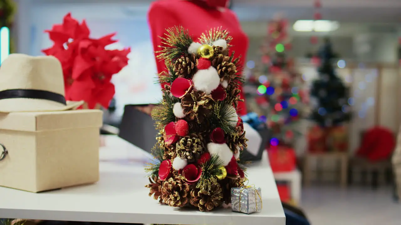 Close up shot of miniature festive Christmas tree crafted from pine cones sitting on clothing store display table next to stylish neckties Xmas decoration in empty fashion shop