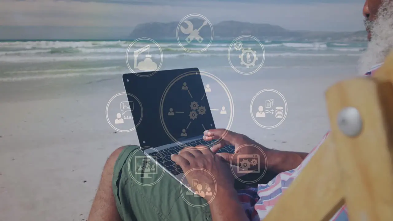 Animation of icons over senior african american man using laptop on sunny beach