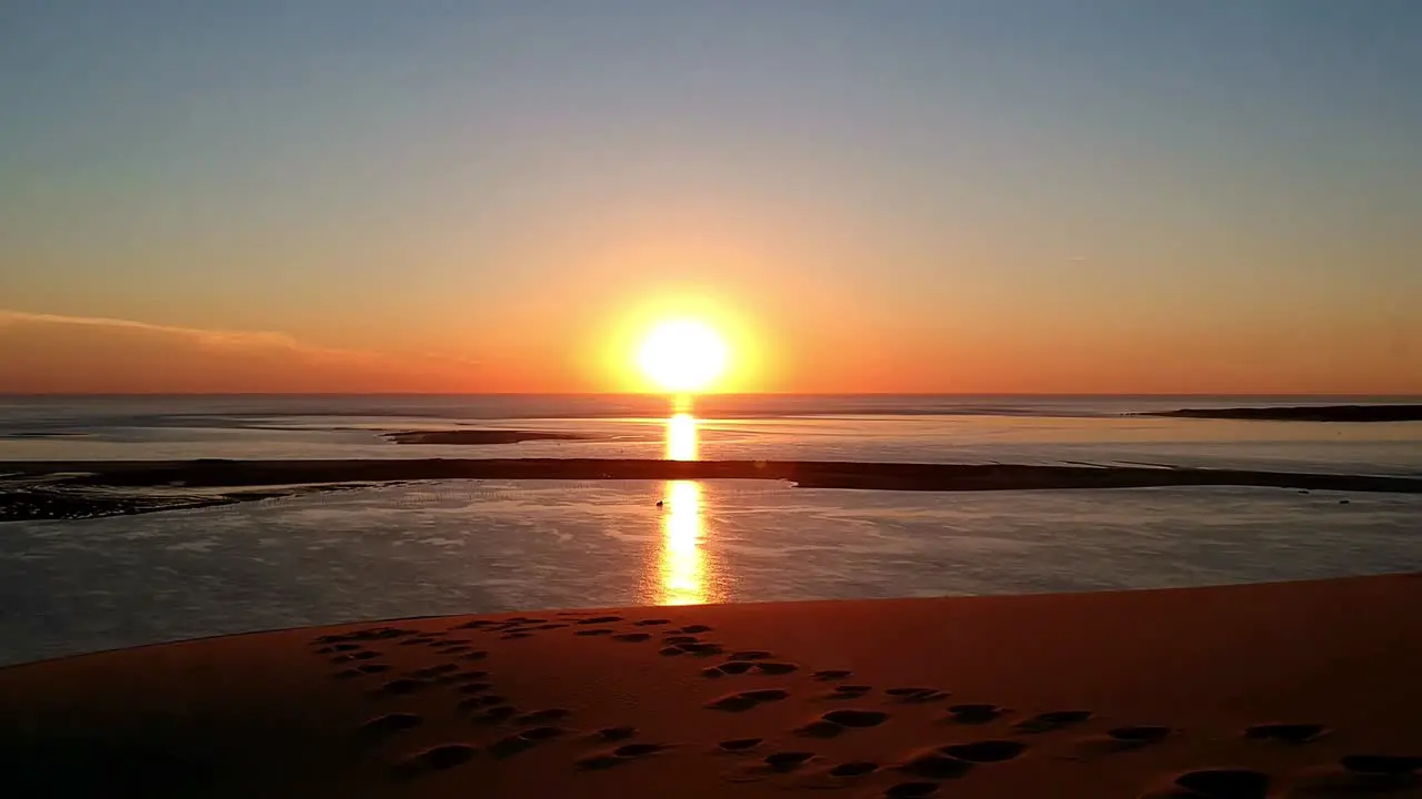 drone video of a beautiful orange sunset on a sand dune with a sea background sand has footprints and looks like pure heaven