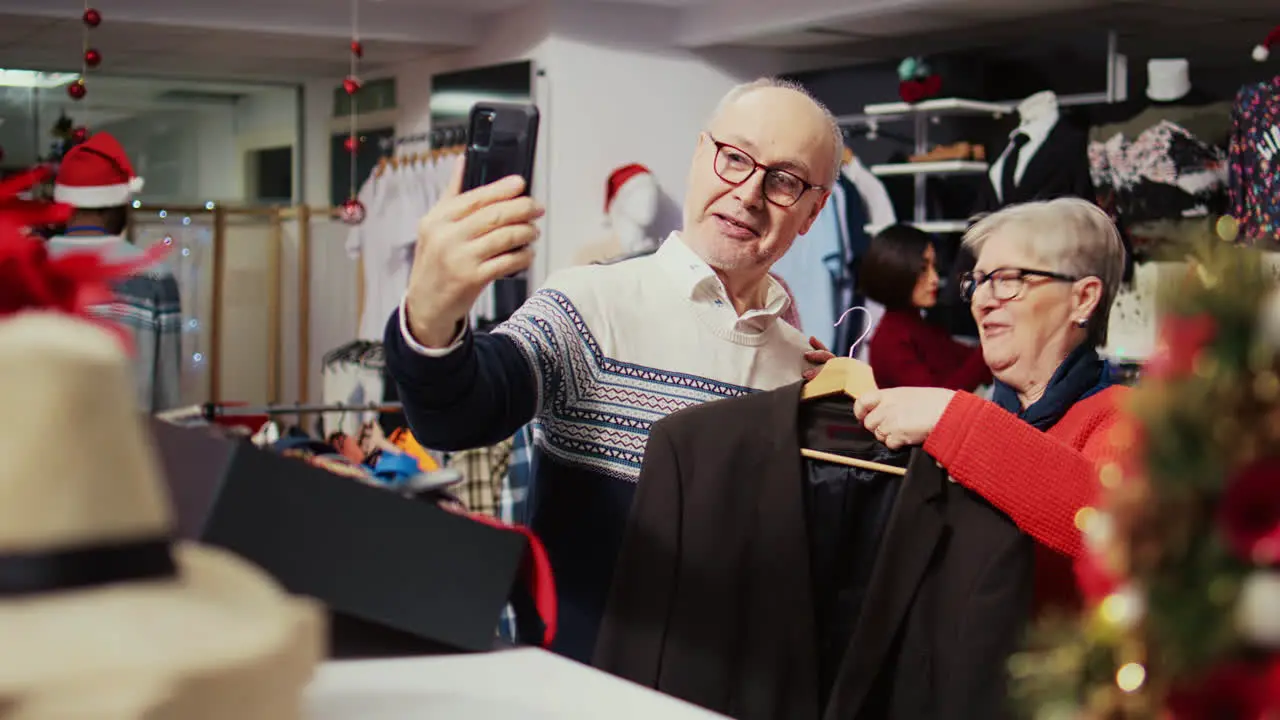 Senior husband and wife in festive ornate fashion shop talking with grandson over online videocall asking him to pick between stylish blazers to buy as gift before xmas family event