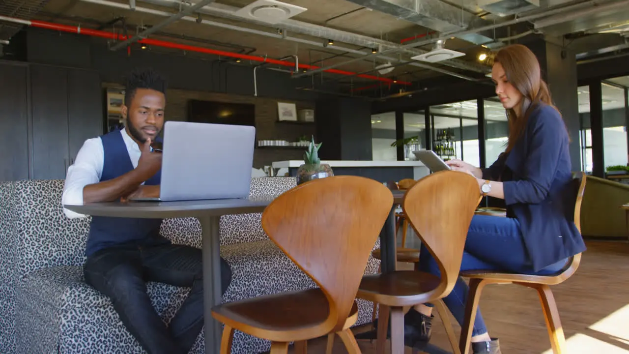 Young cool mixed-race business executives using multimedia devices in cafeteria of modern office 4k